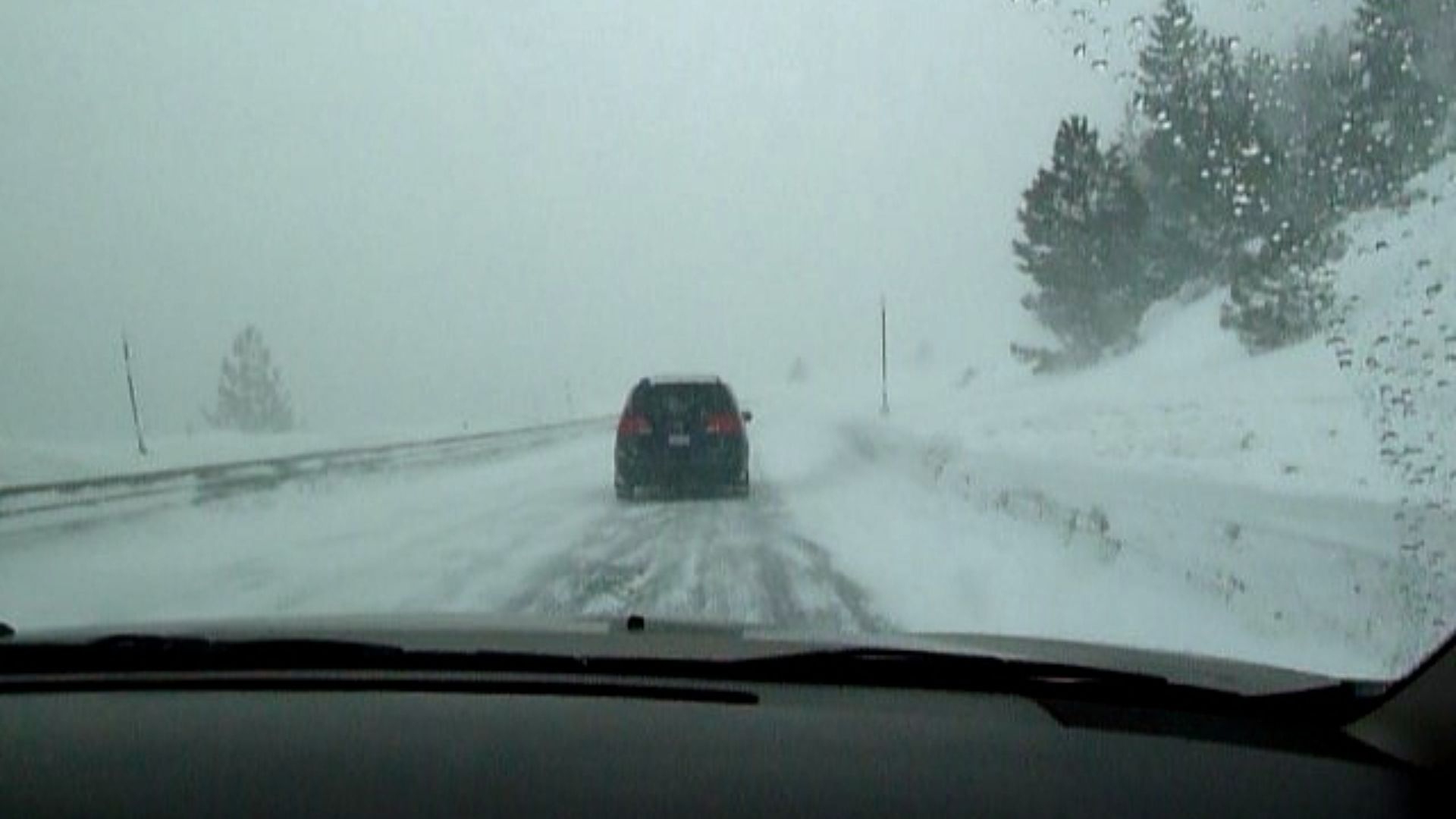 Driving in a snowstorm with cars visible ahead.