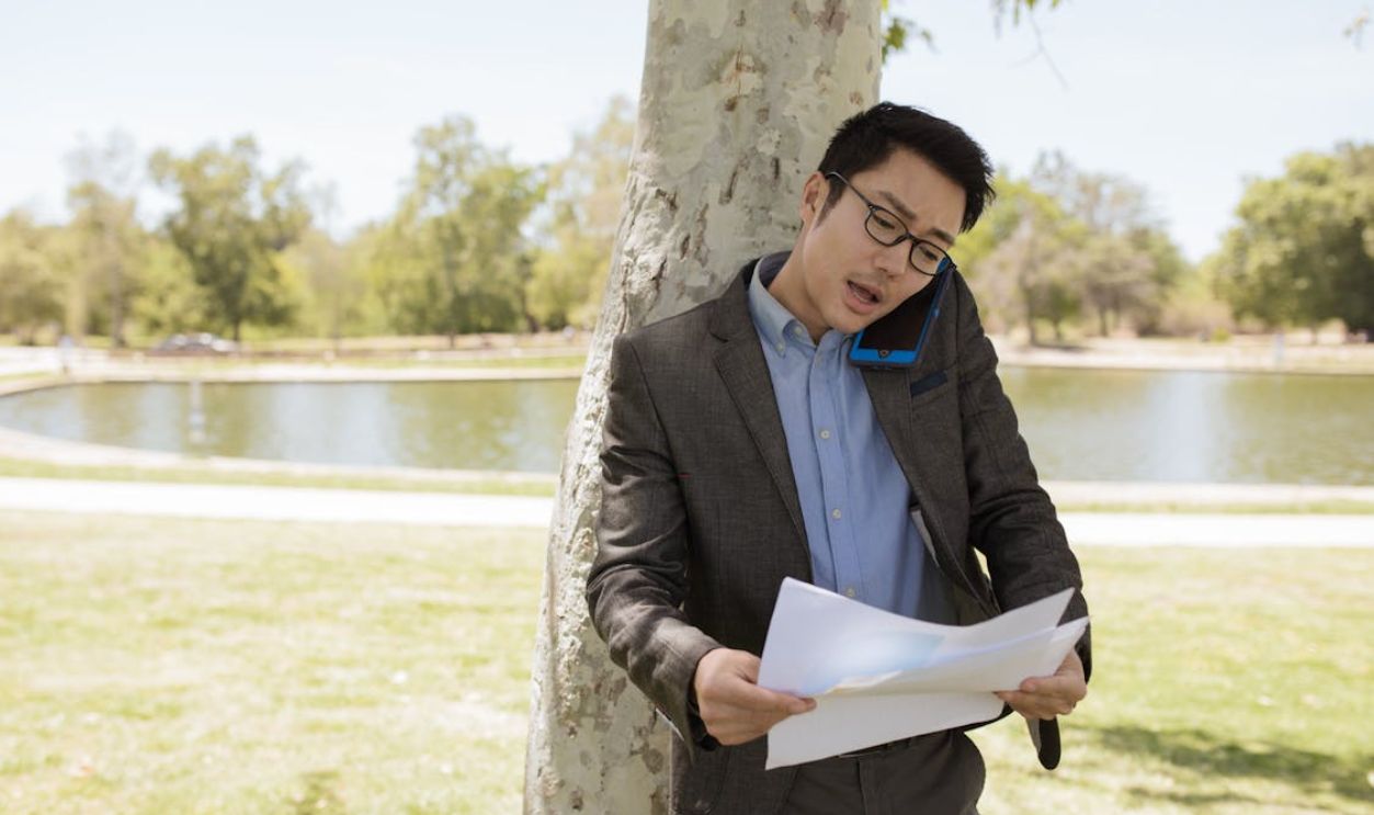 A Man Talking on a Smartphone while Looking at Documents in a Park