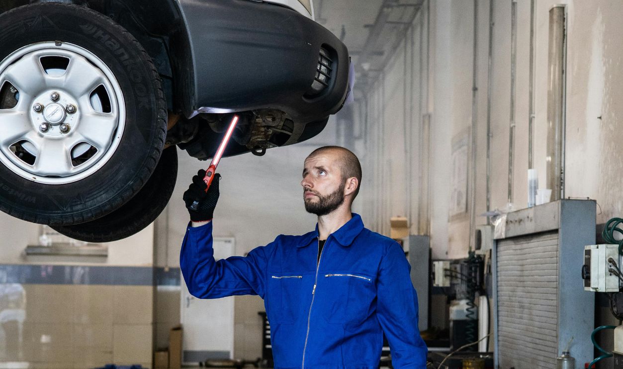 A Serviceman in Blue Coverall Standing Under A Vehicle and Fixing It