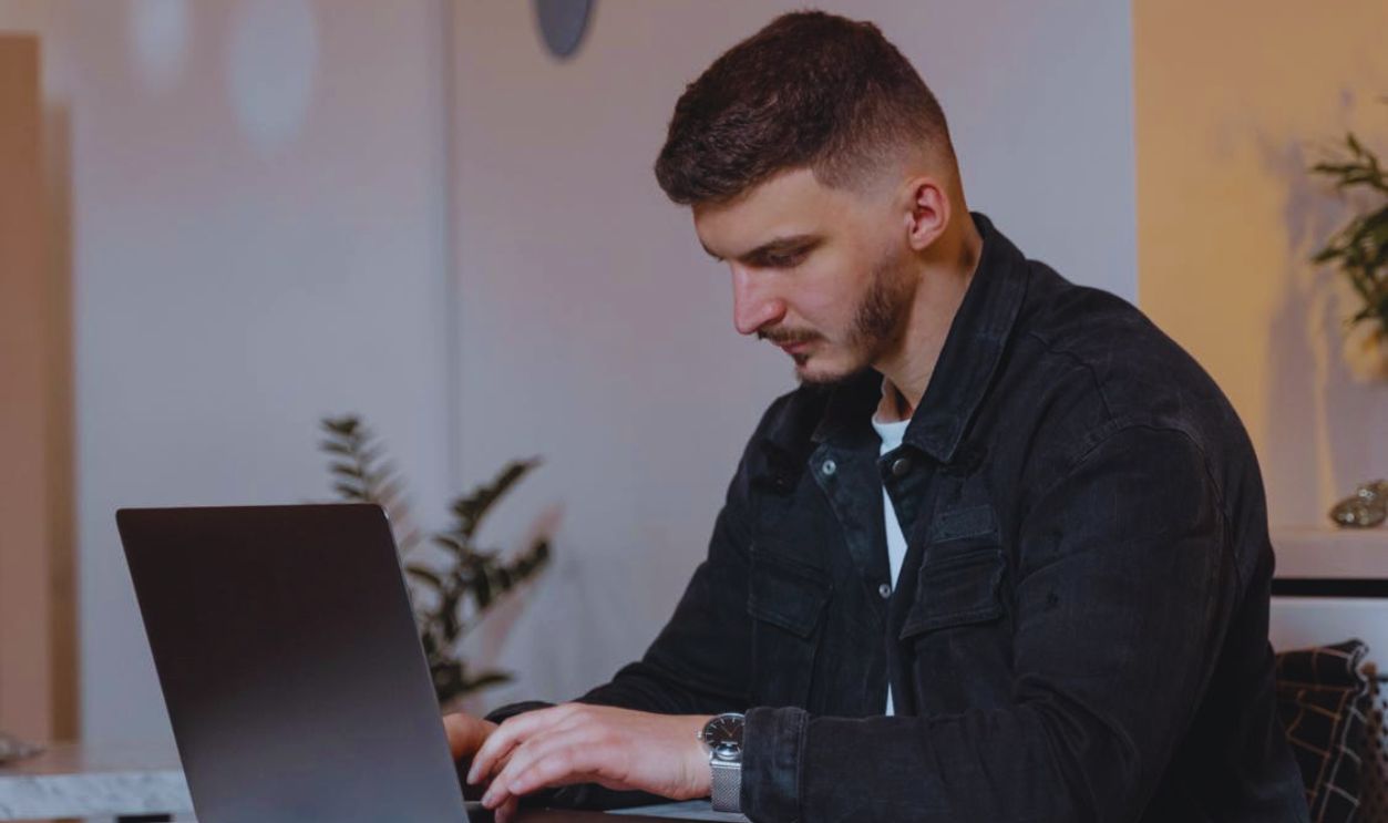 Man in Black Denim Jacket Using Laptop