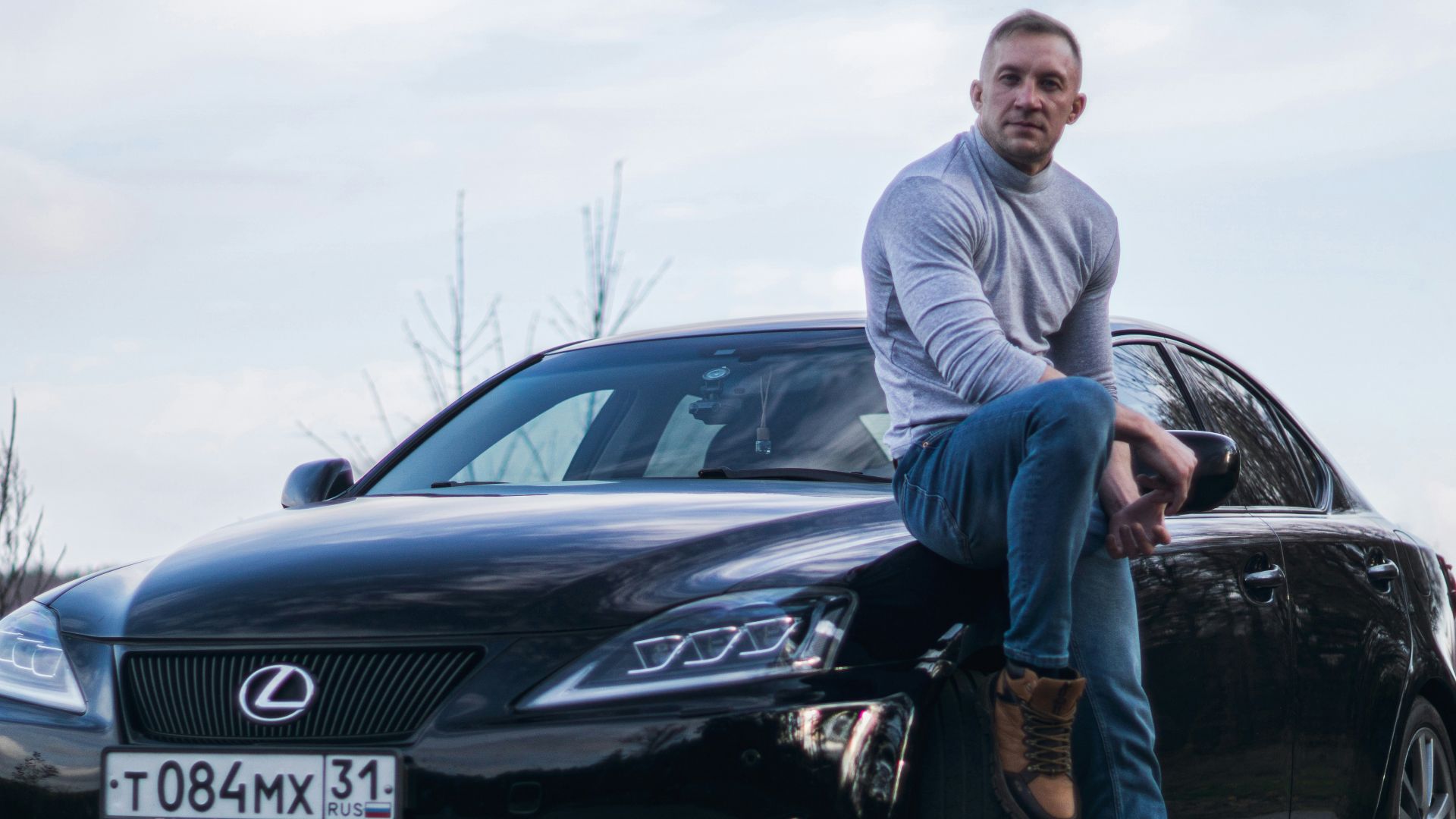 Man leaning on a black lexus sedan outdoors.