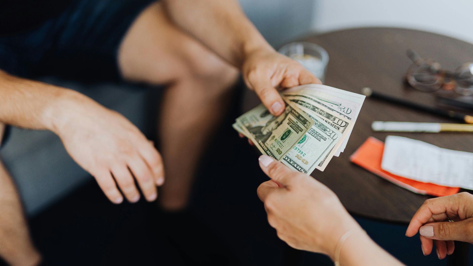 Close-up of hands exchanging US dollar bills, symbolizing a financial transaction or payment.