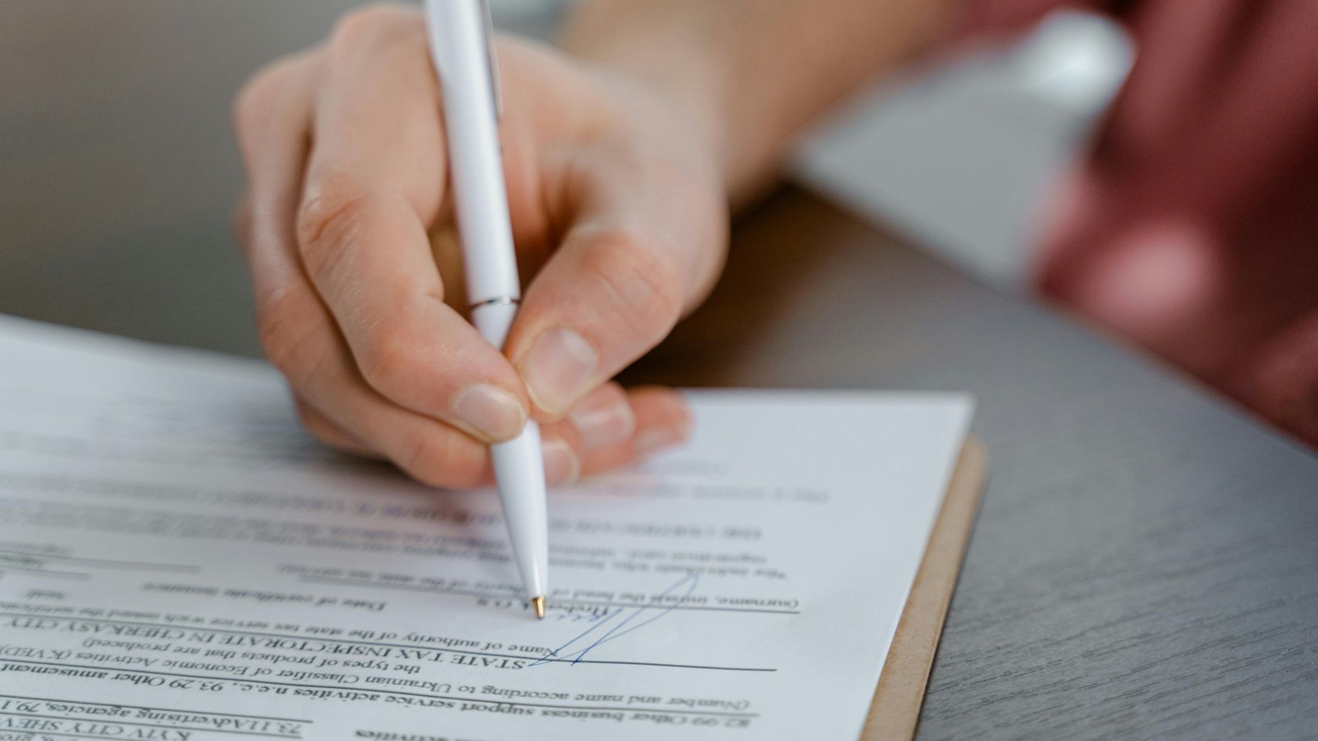 Detailed view of a hand writing a signature on an official document with a ballpoint pen.
