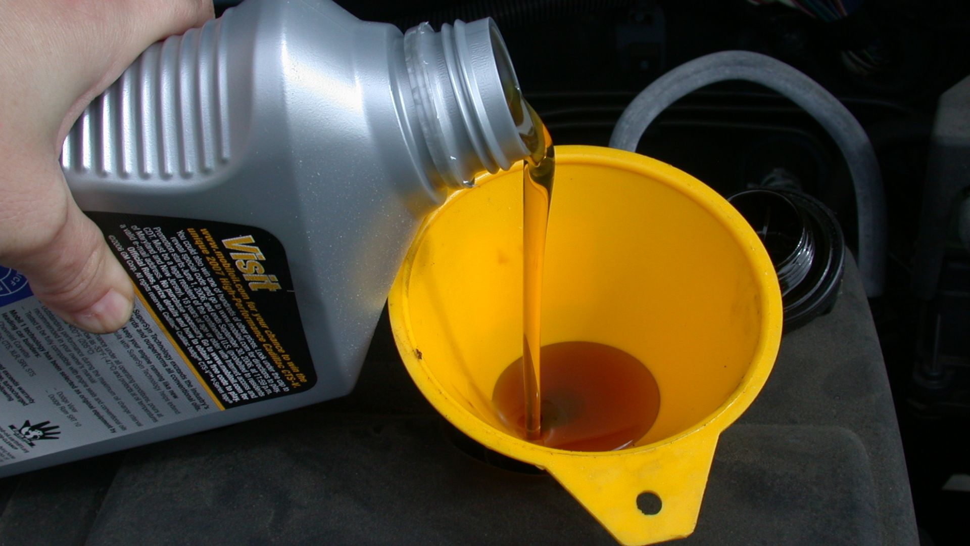 Using a funnel to refill the motor oil in an automobile as part of an oil change.
