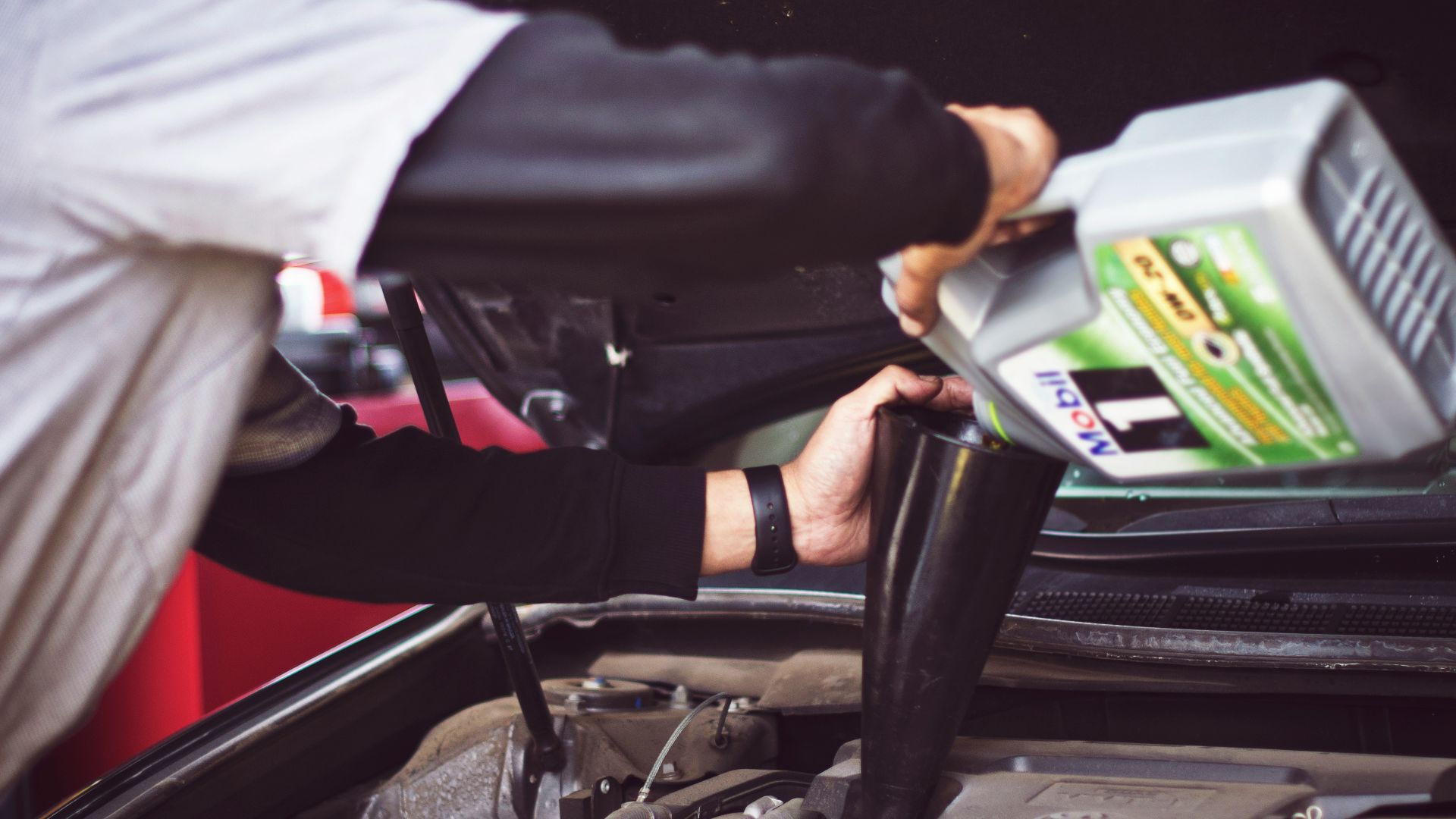 man refilling motor oil on car engine bay
