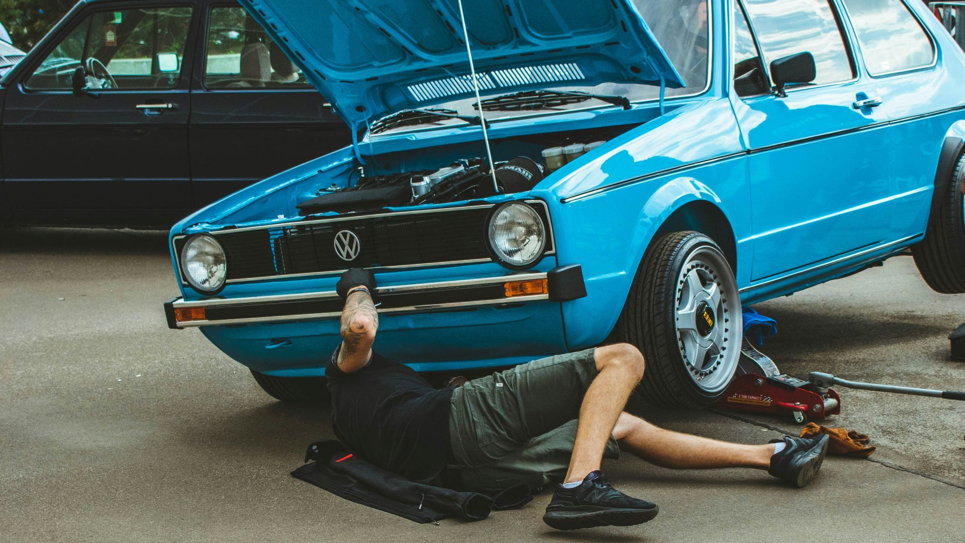a man laying on the ground next to a blue car
