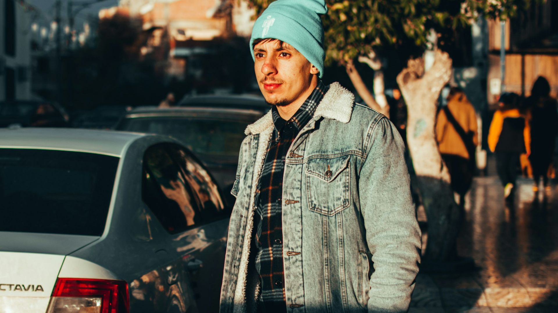 man in blue denim jacket standing beside white car during daytime