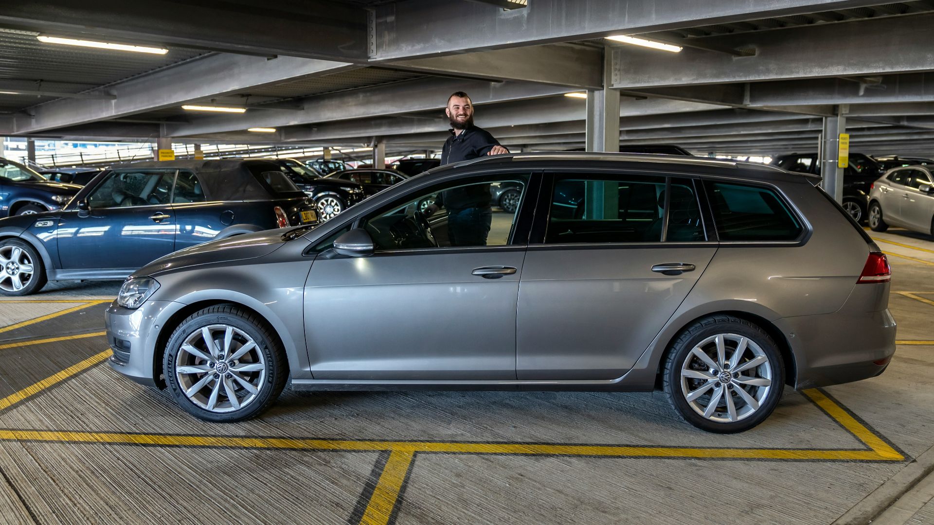 Man standing by a silver station wagon in parking garage