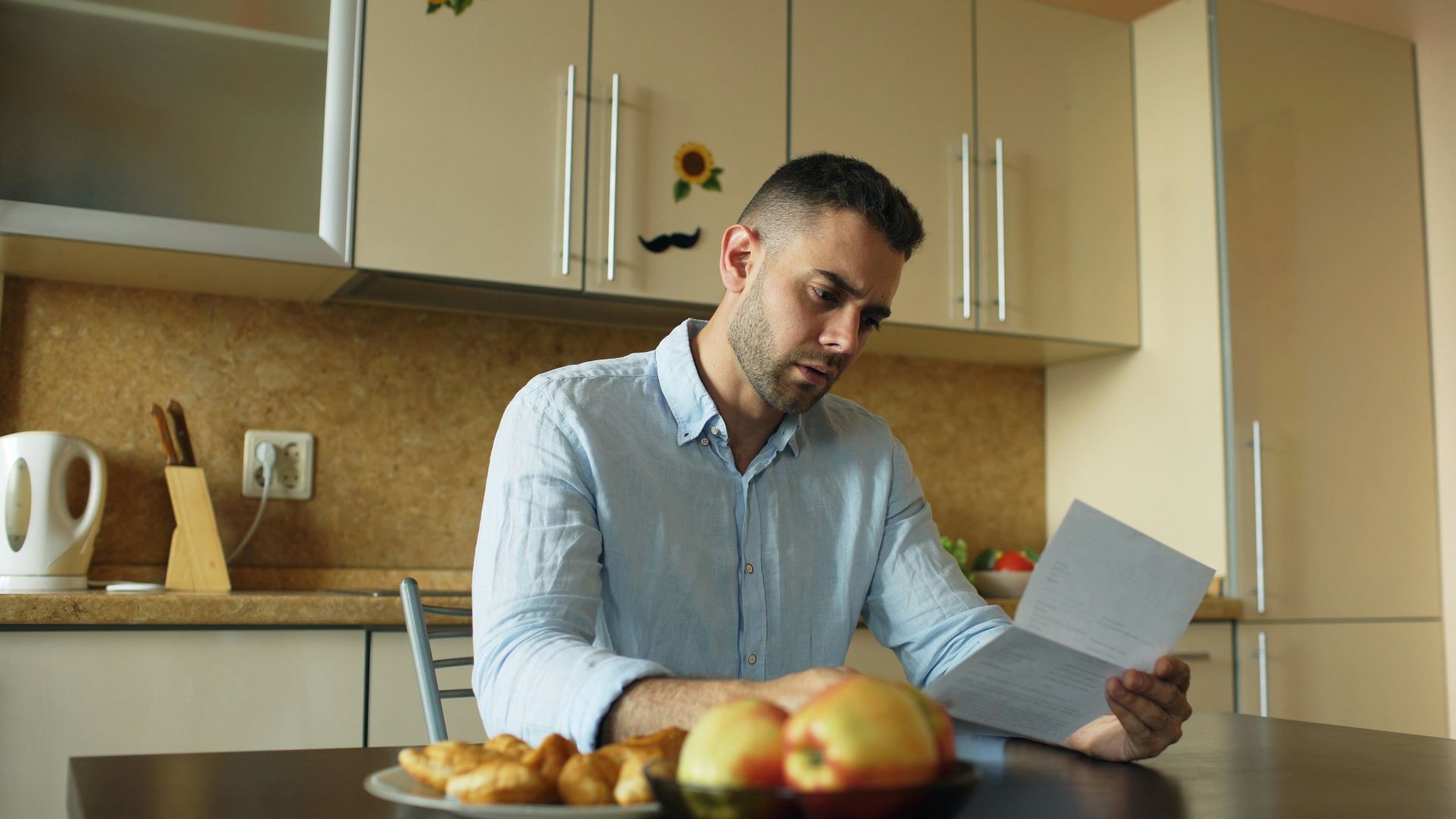 Man reading document at kitchen table with fruit and fruit