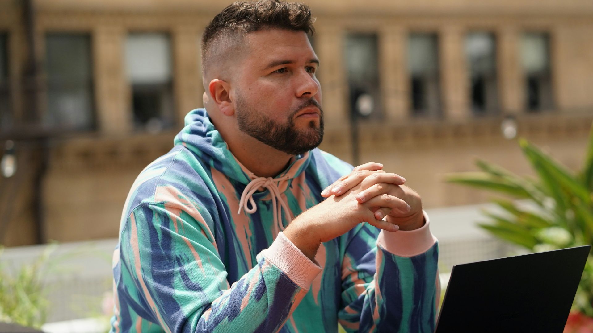 man in blue and white tribal print hoodie sitting beside black laptop computer