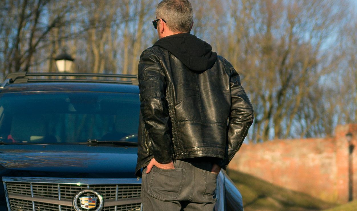 A Man in a Leather Jacket Looking at a Black Cadillac