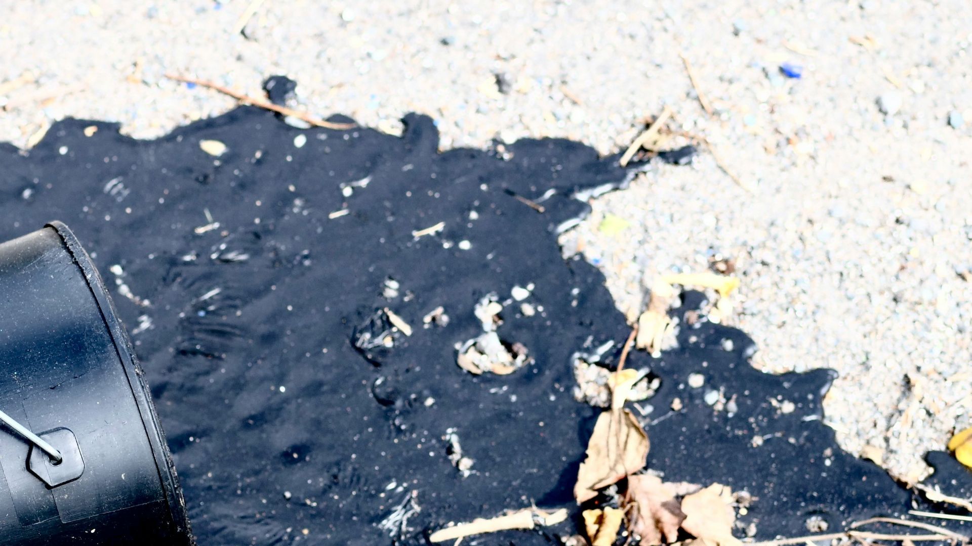 A black bucket spills dark liquid onto the ground.