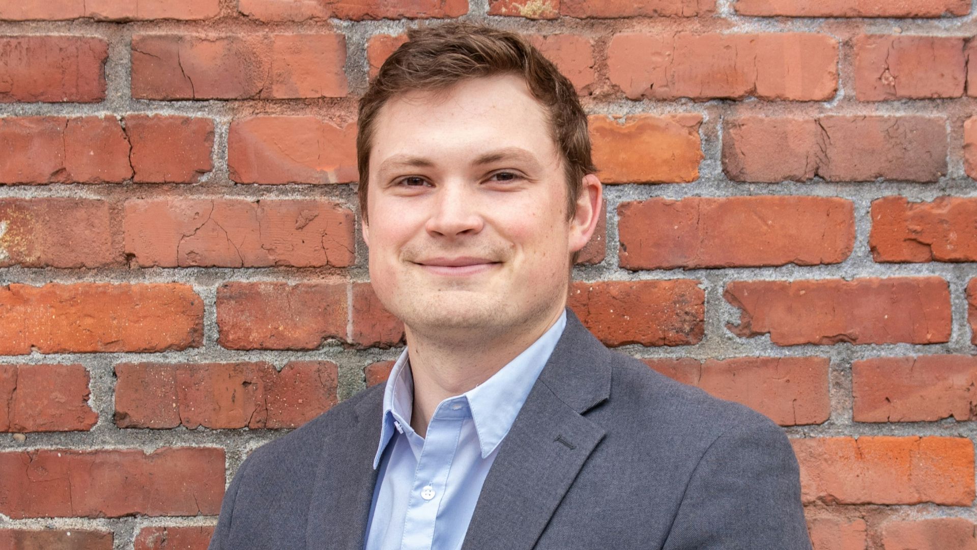 man in gray suit jacket standing beside brown brick wall