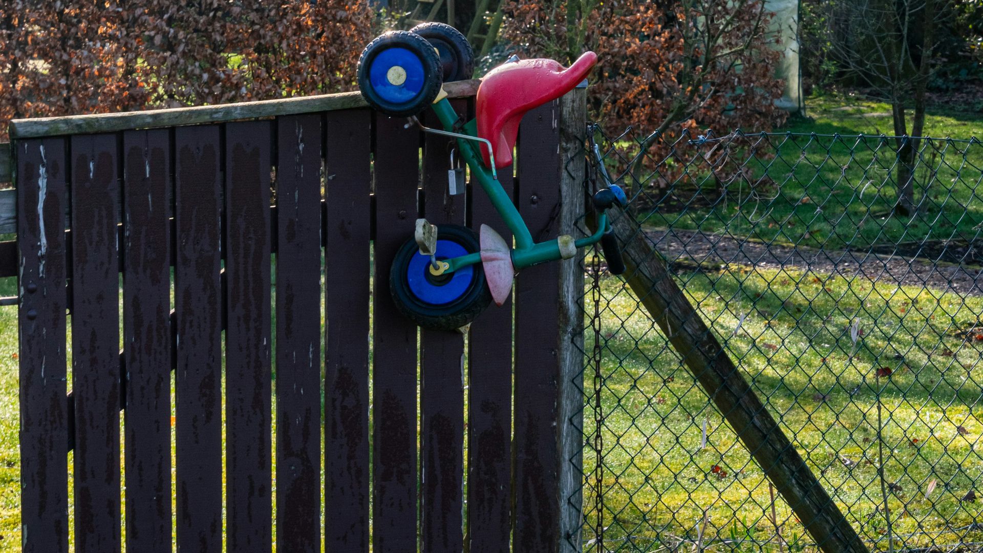 A child's tricycle rests on a wooden fence.