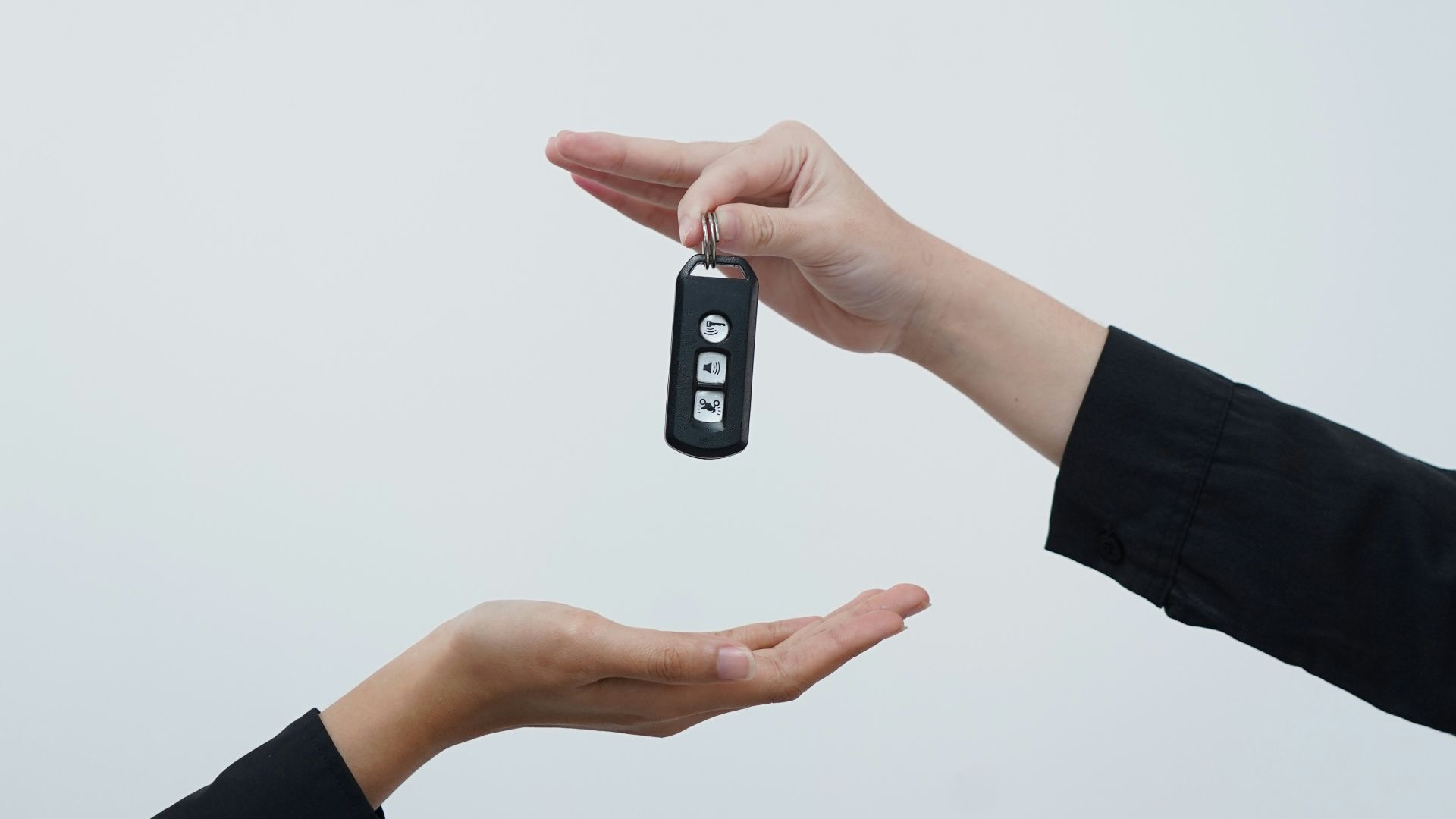 Hands exchanging a car key against a light background