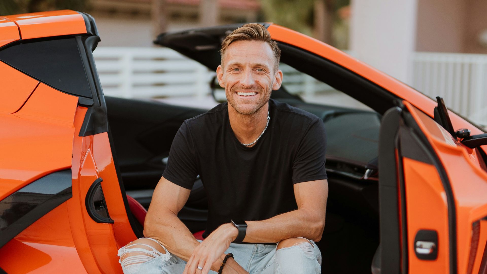 a man sitting in the open door of an orange sports car