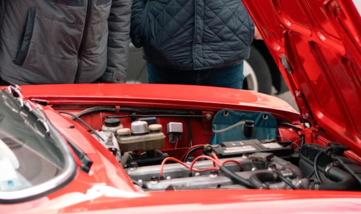 two men looking under the hood of a red car