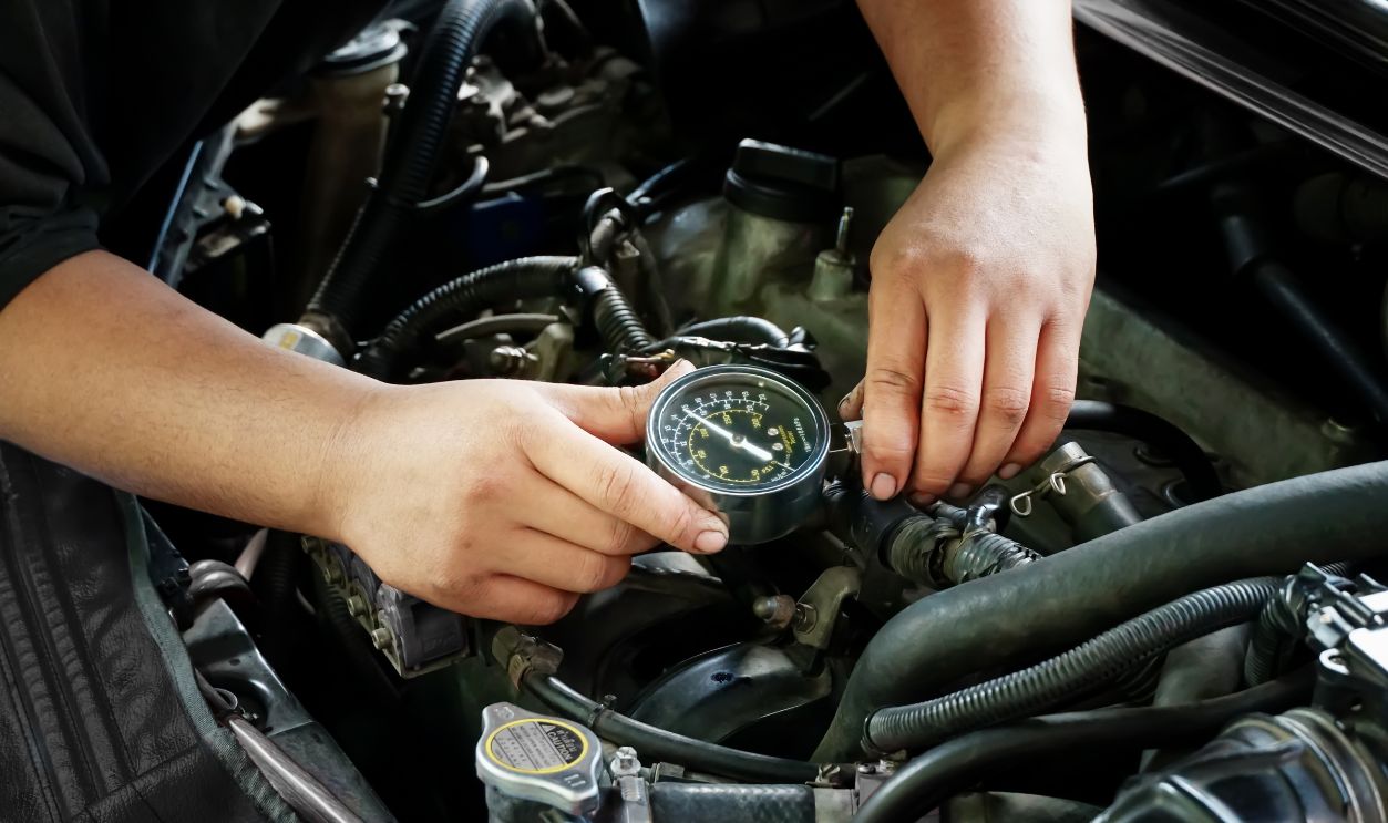 Male mechanic measures the compression in the cylinder of a car engine using a barometer and repair in a workshop for vehicles. Auto service industry. engine compression tester. 