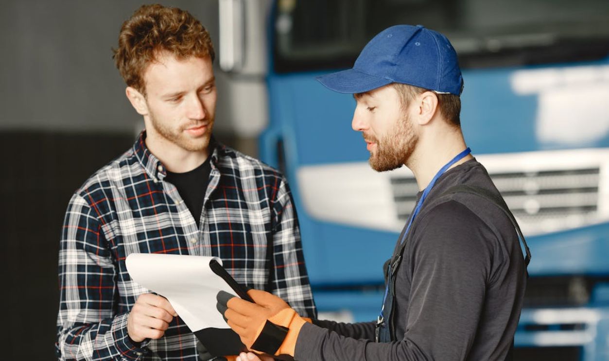 Man in Black Uniform and Blue Cap Holding White Paper Beside Man in Plaid Shirt