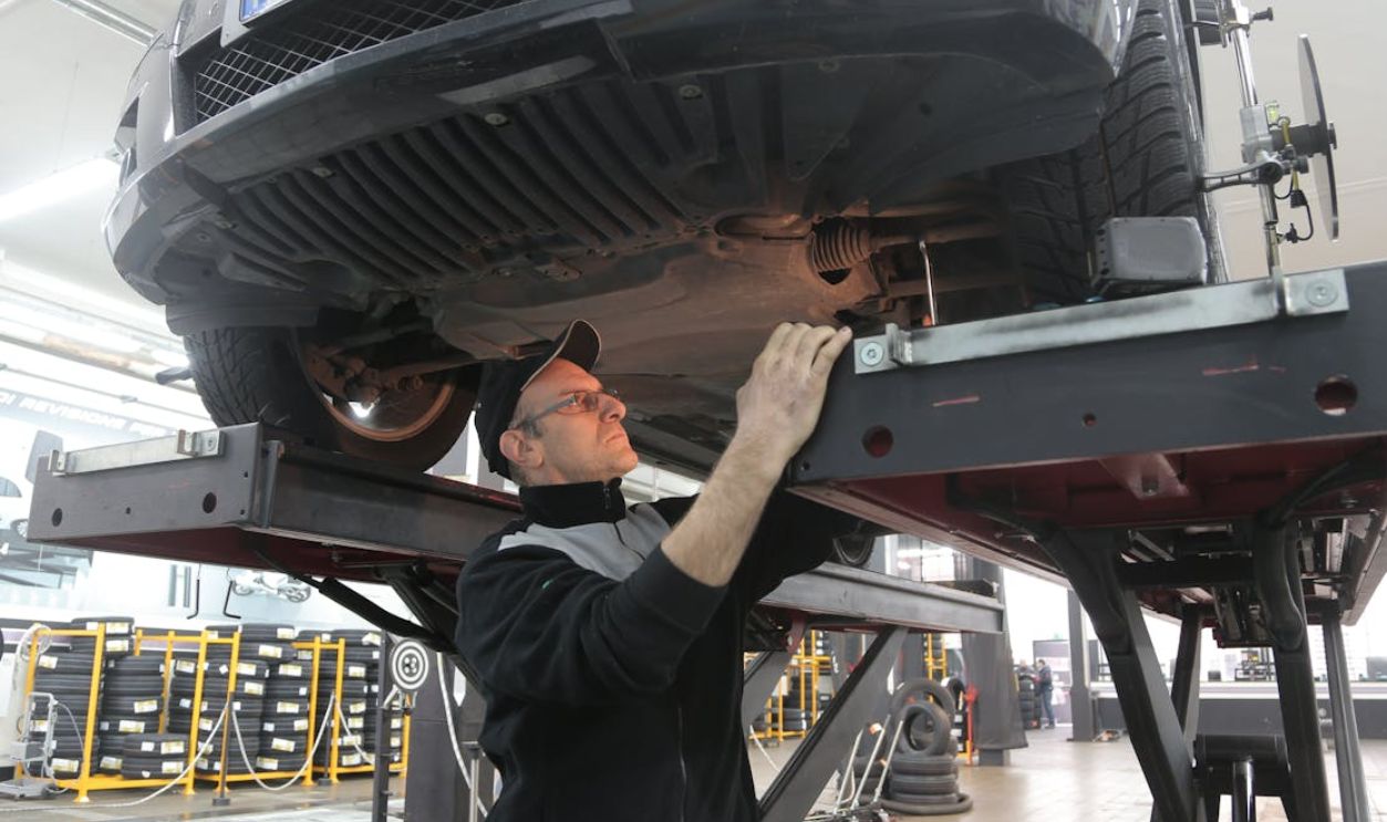 Man in Black Jacket Standing Under the Vehicle