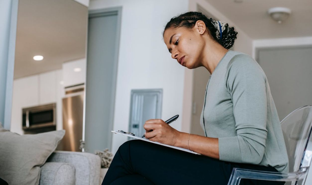 Concentrated ethnic female interviewer or psychotherapist taking notes in clipboard