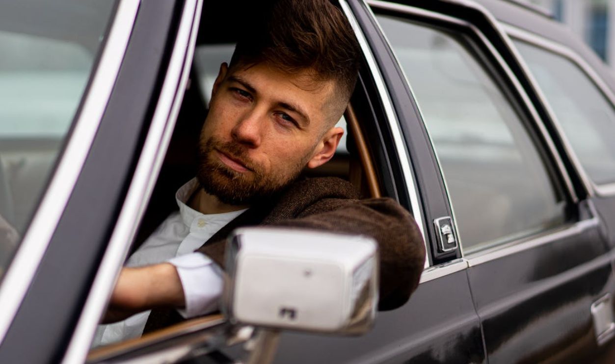 Confident man with trendy hairstyle on vintage car