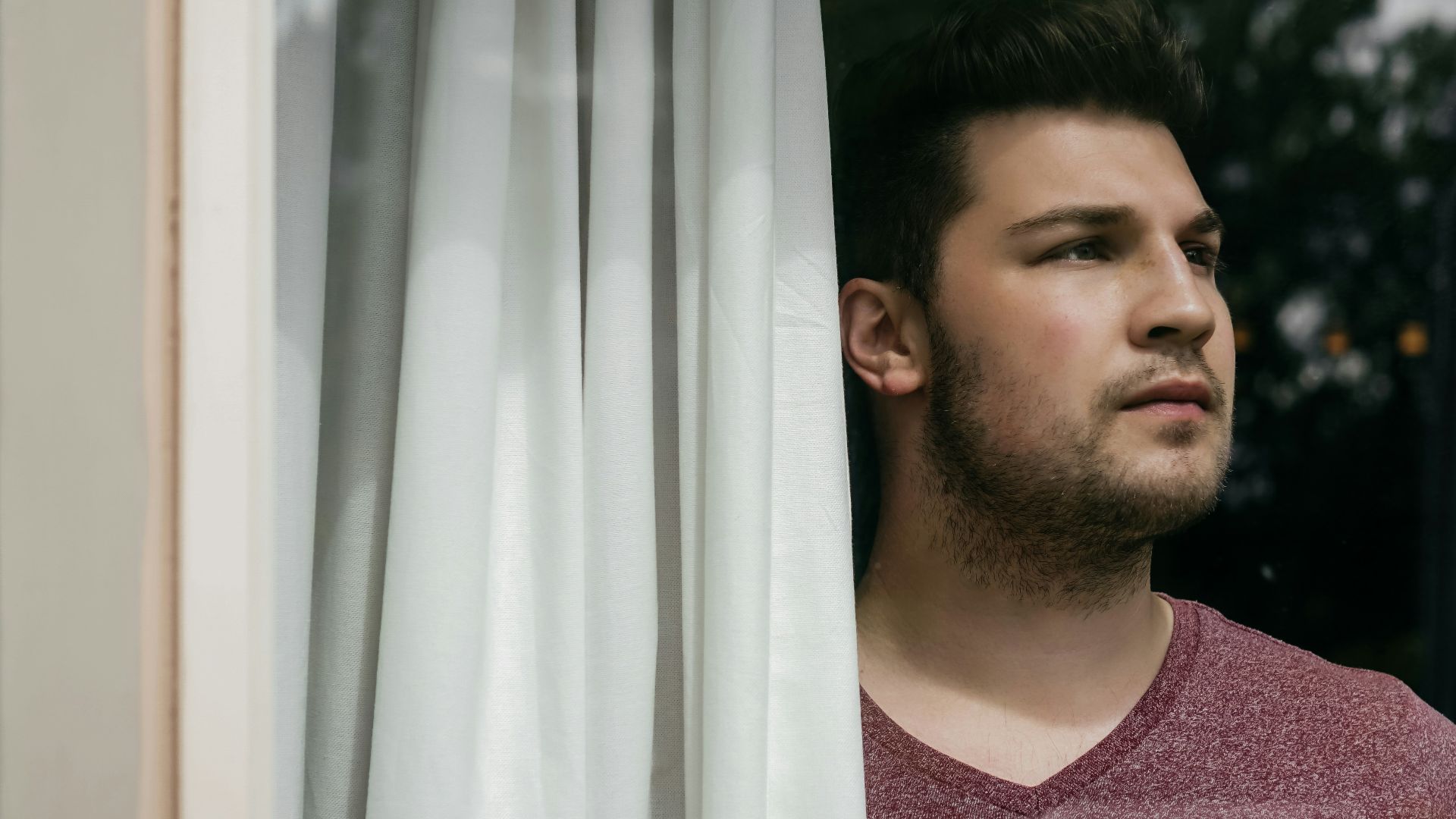 man in red crew neck shirt standing beside white curtain