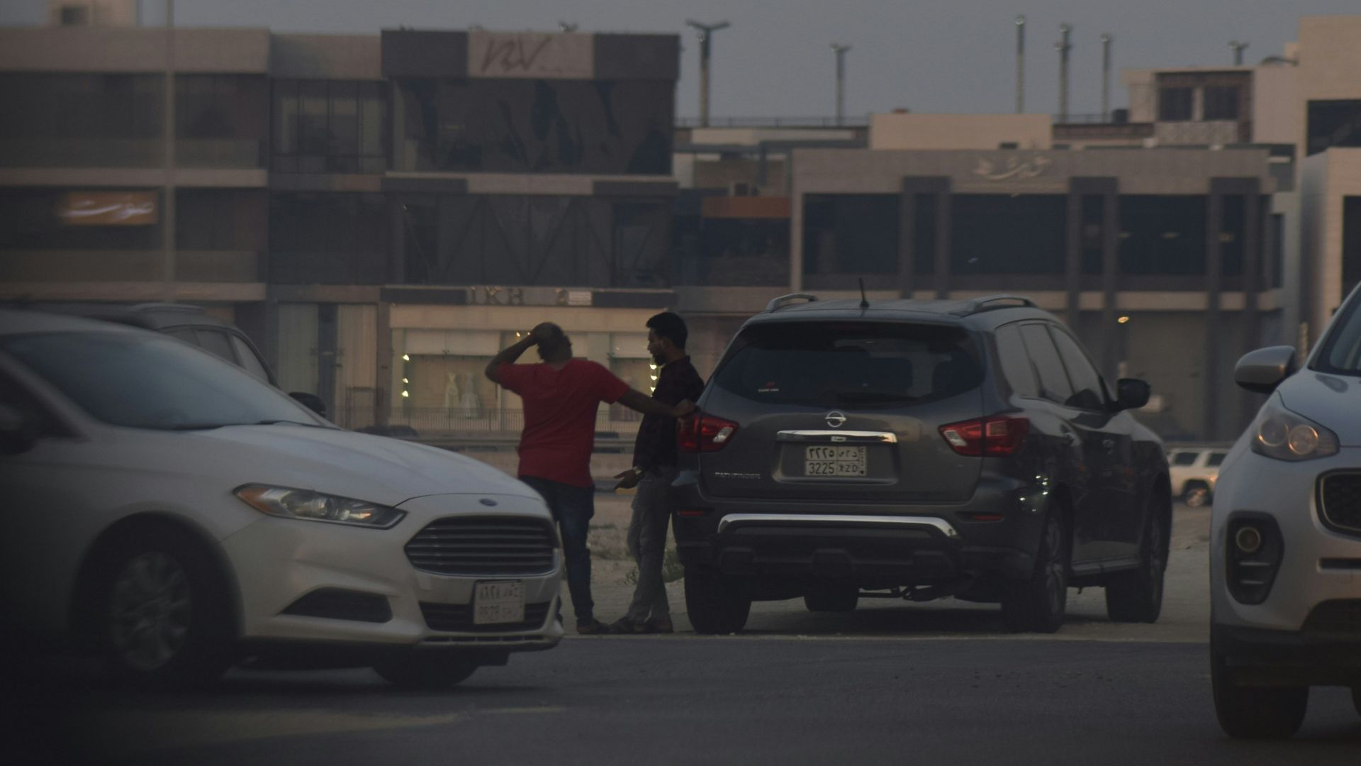 Two men standing between cars on a street.