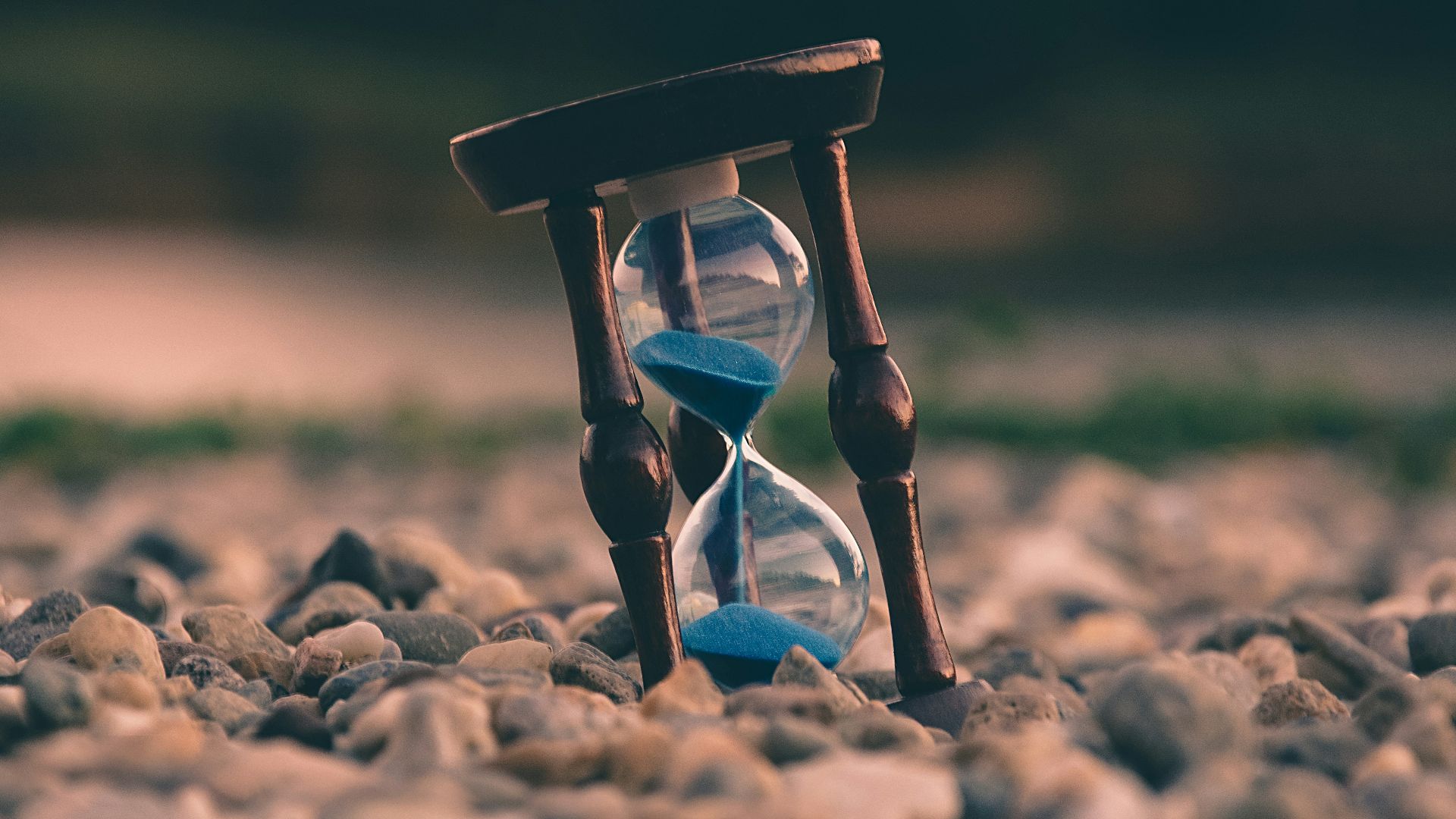 selective focus photo of brown and blue hourglass on stones