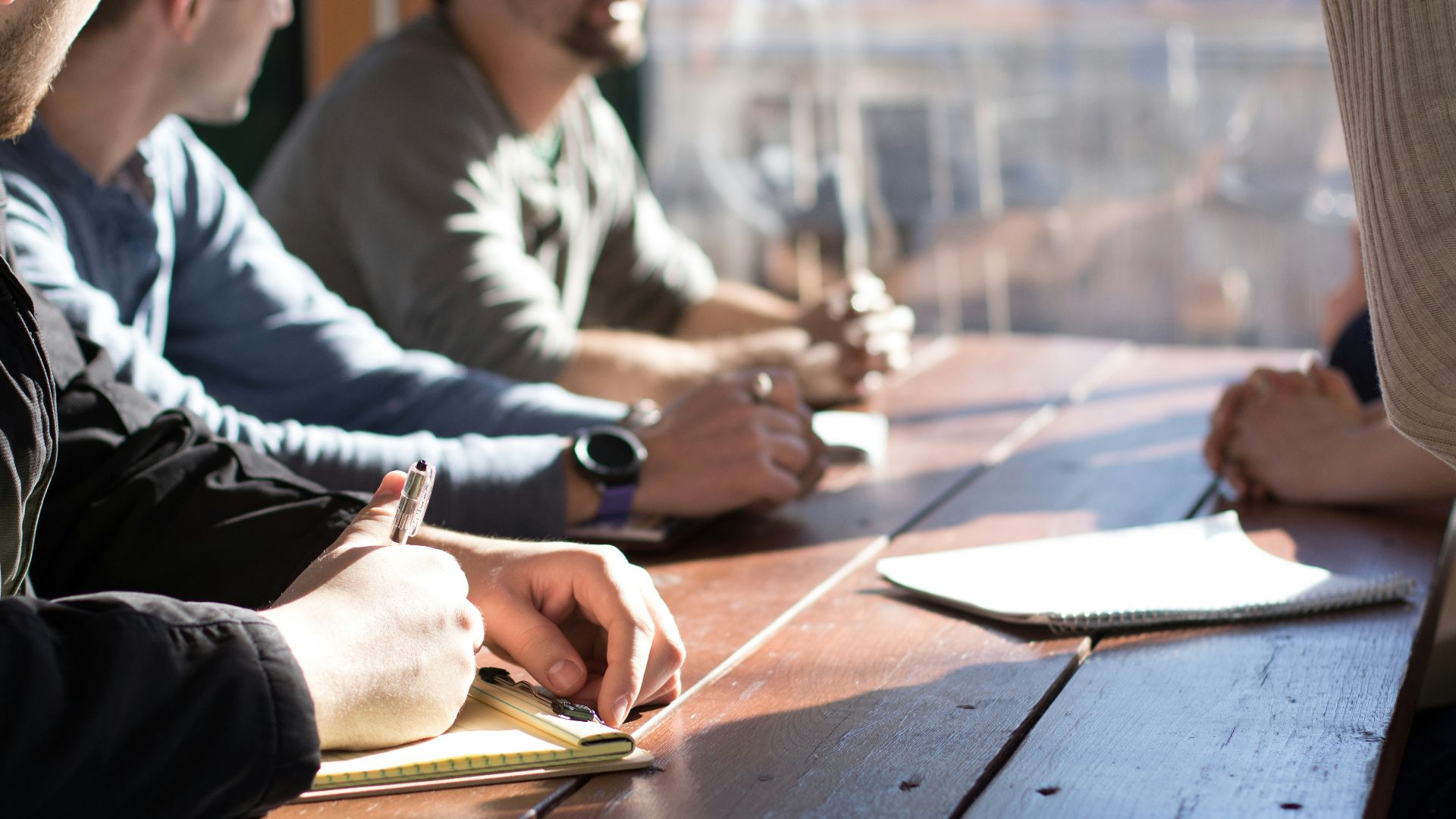 people sitting on chair in front of table while holding pens during daytime