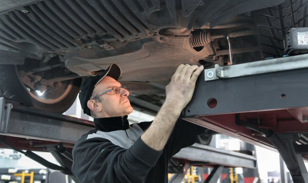 Man in Black Jacket Standing Under the Vehicle