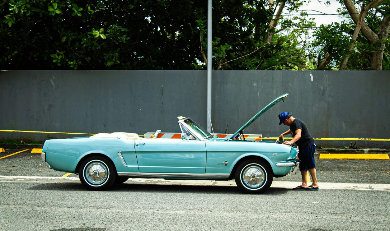Man Inspecting Classic Blue Convertible on Street