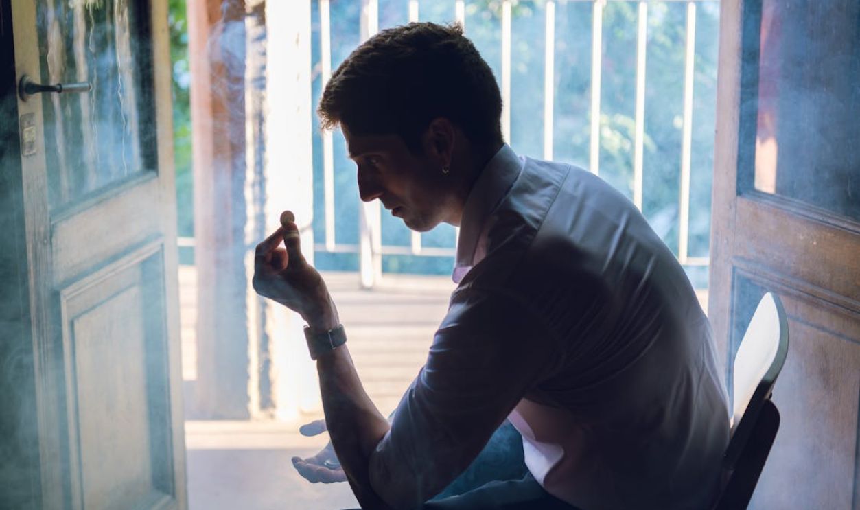 Pensive Man Holding Coin by Sunlit Balcony