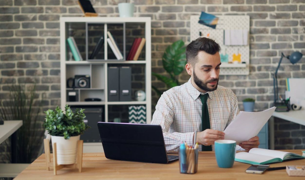 Man in Shirt Sitting at Office and Reading Document