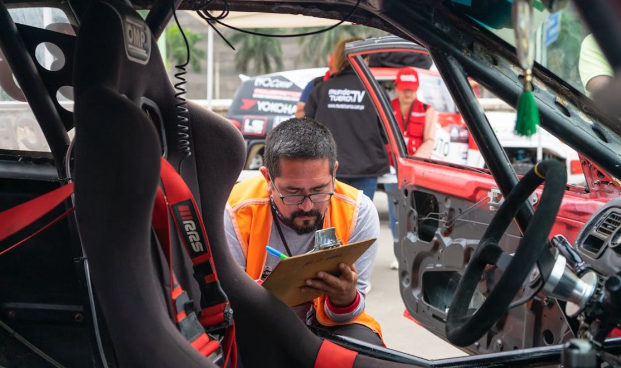 A Man Crouching near a Race Car Writing on a Piece of Paper
