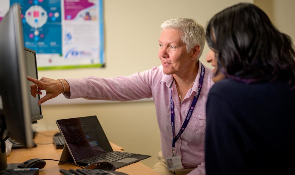 Young and Elderly Woman Sitting at a Desk and Looking at a Computer Monitor