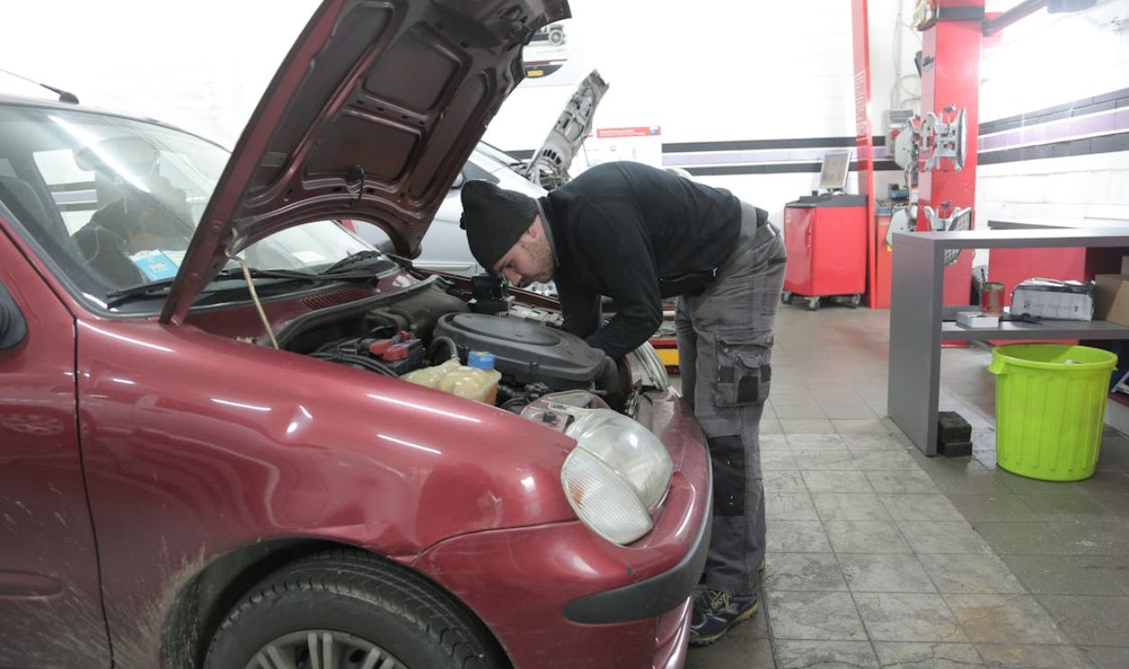 Man in Black Jacket and Cargo Pants Standing Beside Red Car