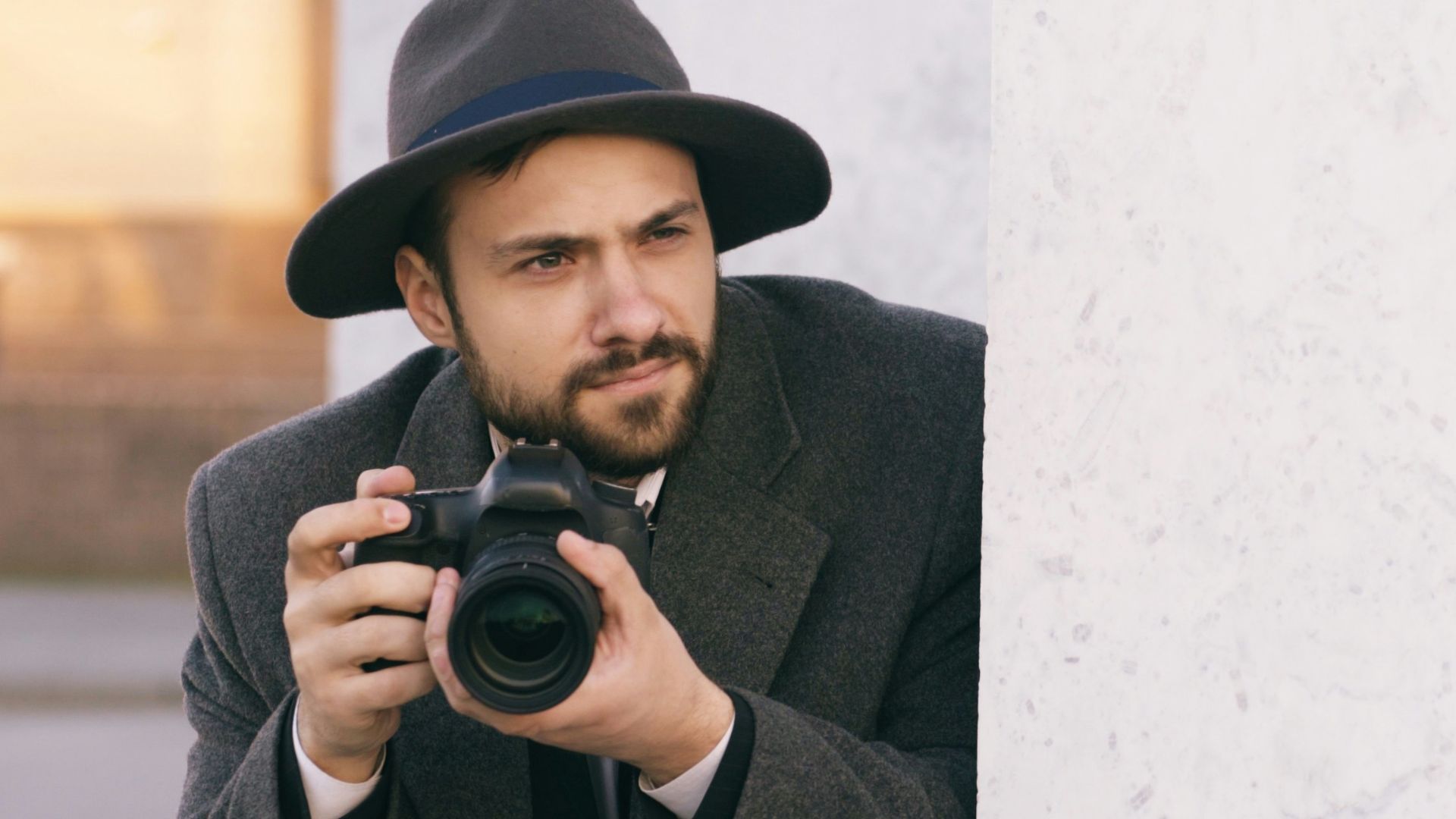 Man in hat holding camera behind wall