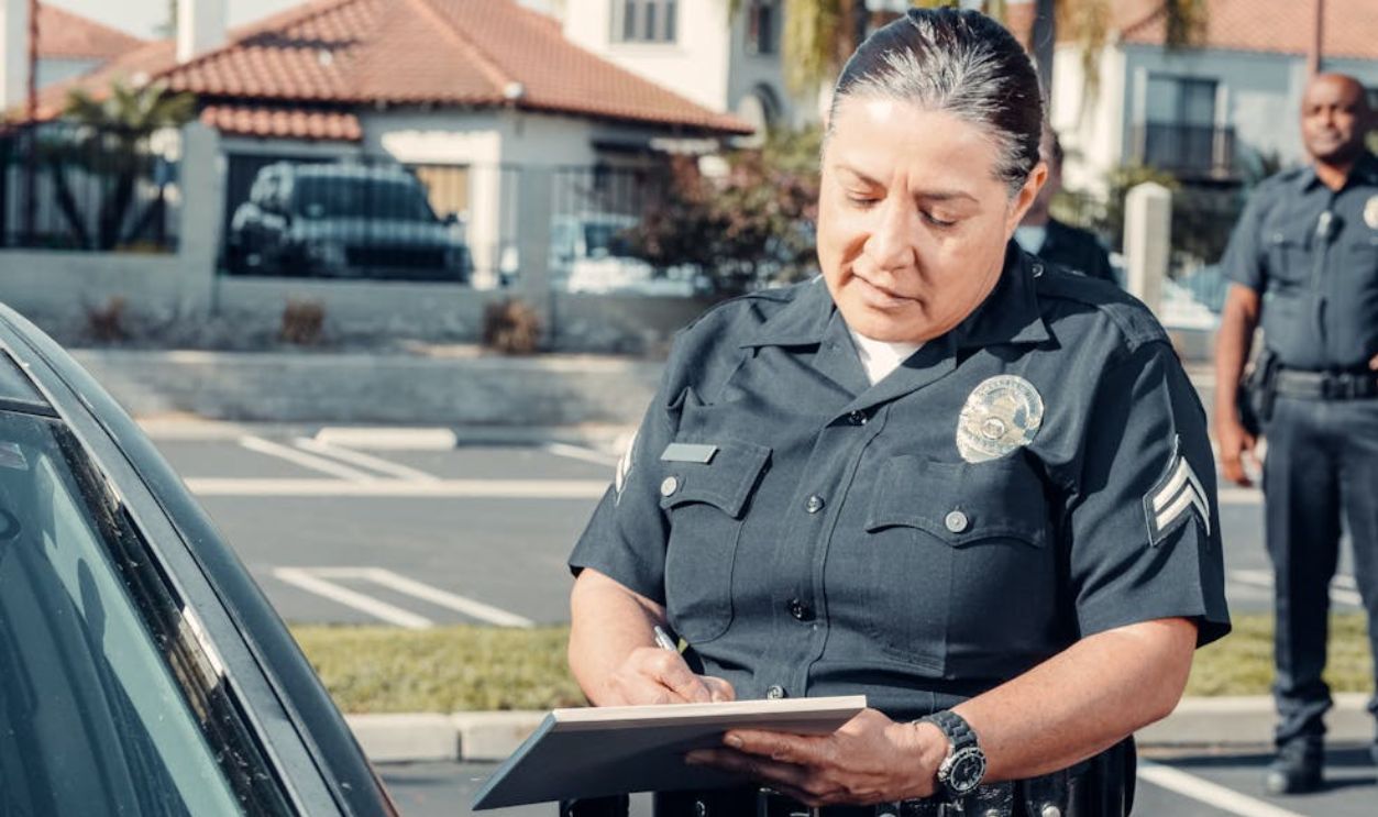 A Police Officer Standing Beside a Car while Holding a Clipboard