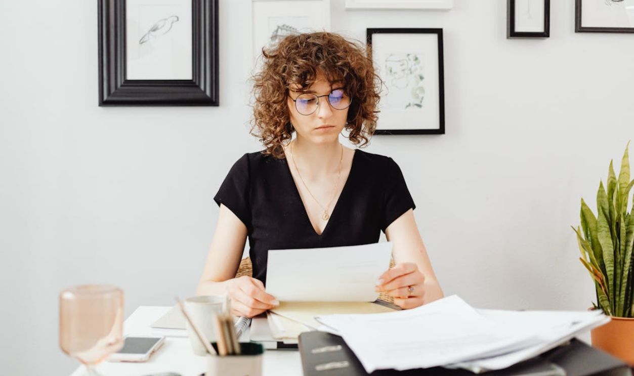 Curly-Haired Woman Wearing Eyeglasses while Holding a Paper