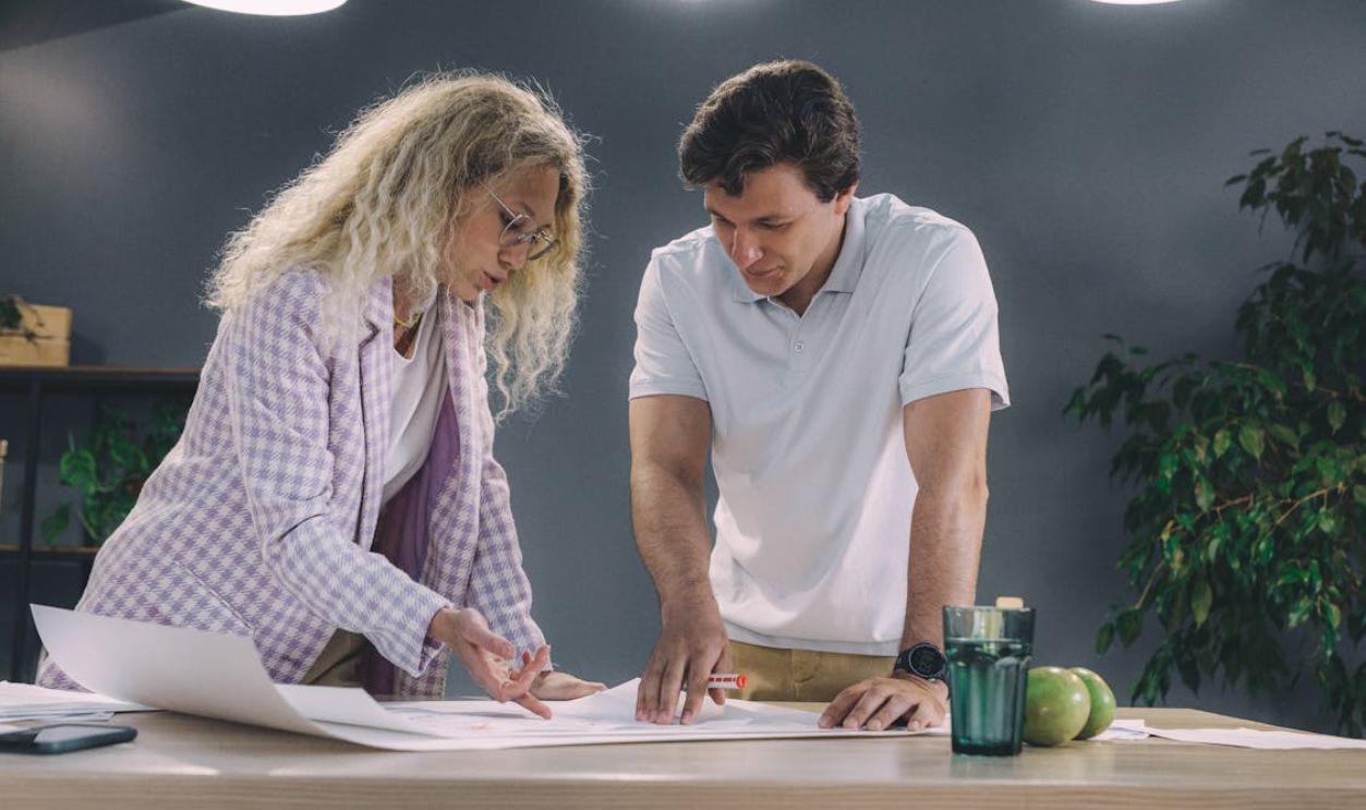 Man and Woman Leaning over a Table and Working on a Project