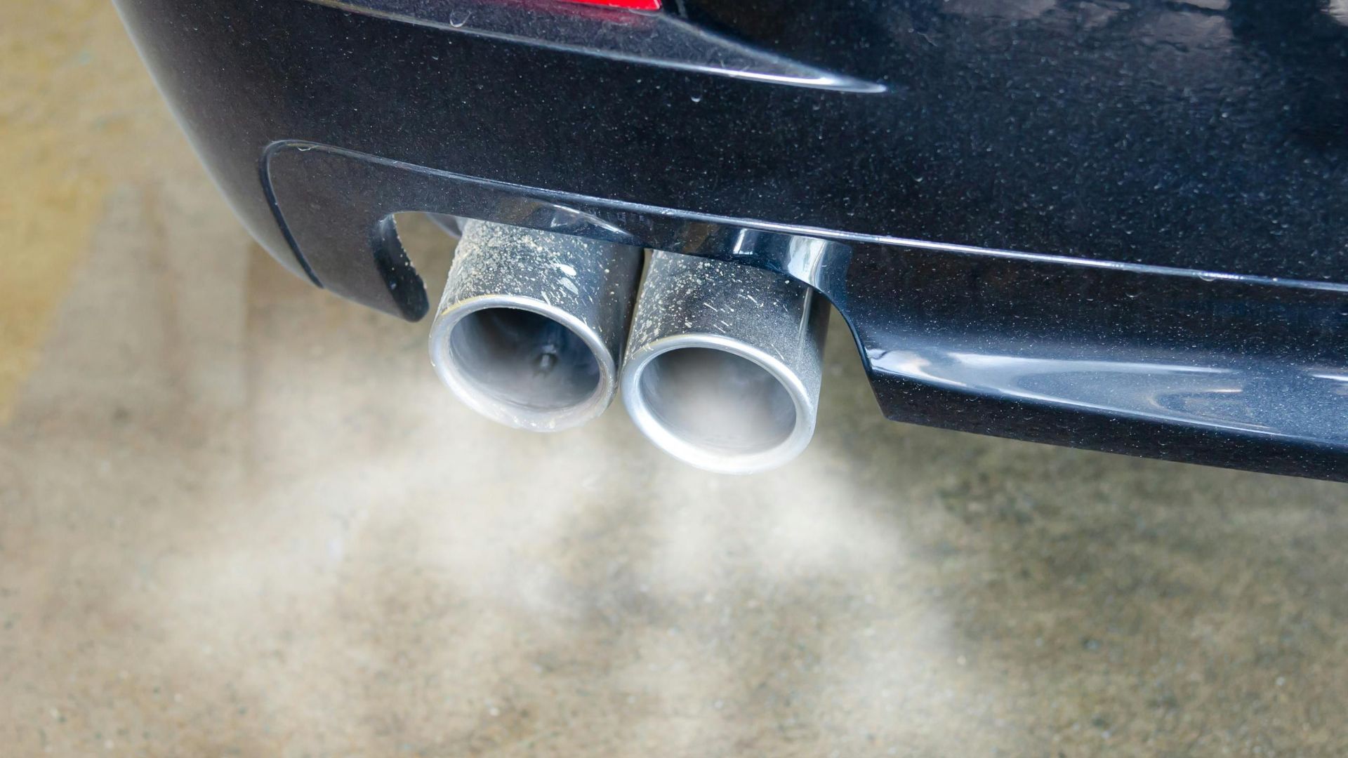 Close-up of a car's exhaust pipes emitting visible smoke, highlighting air pollution.