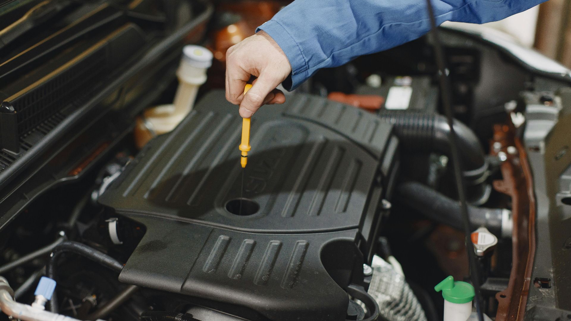 Close-up of a person checking engine oil using a dipstick in a car's engine bay.