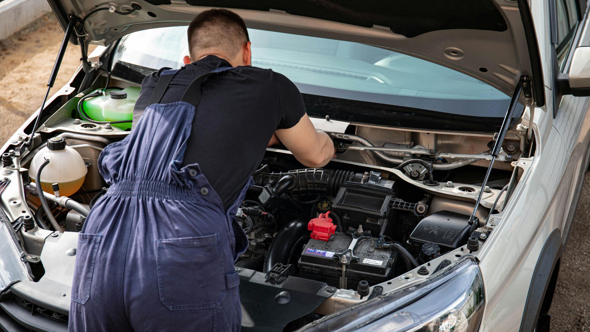 Close-up of mechanic repairing a car engine. Outdoor setting during the day.