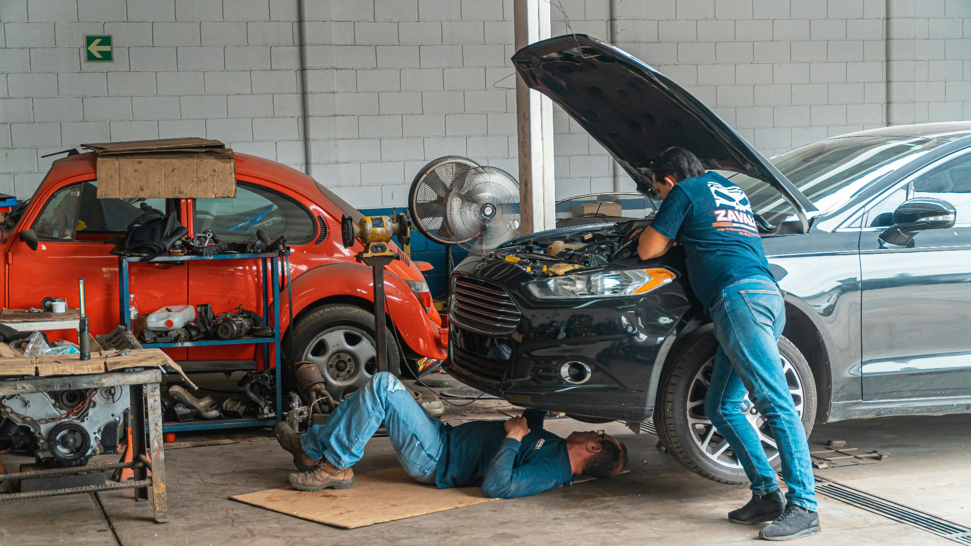 Mechanics working in an automotive workshop, repairing cars and performing maintenance.