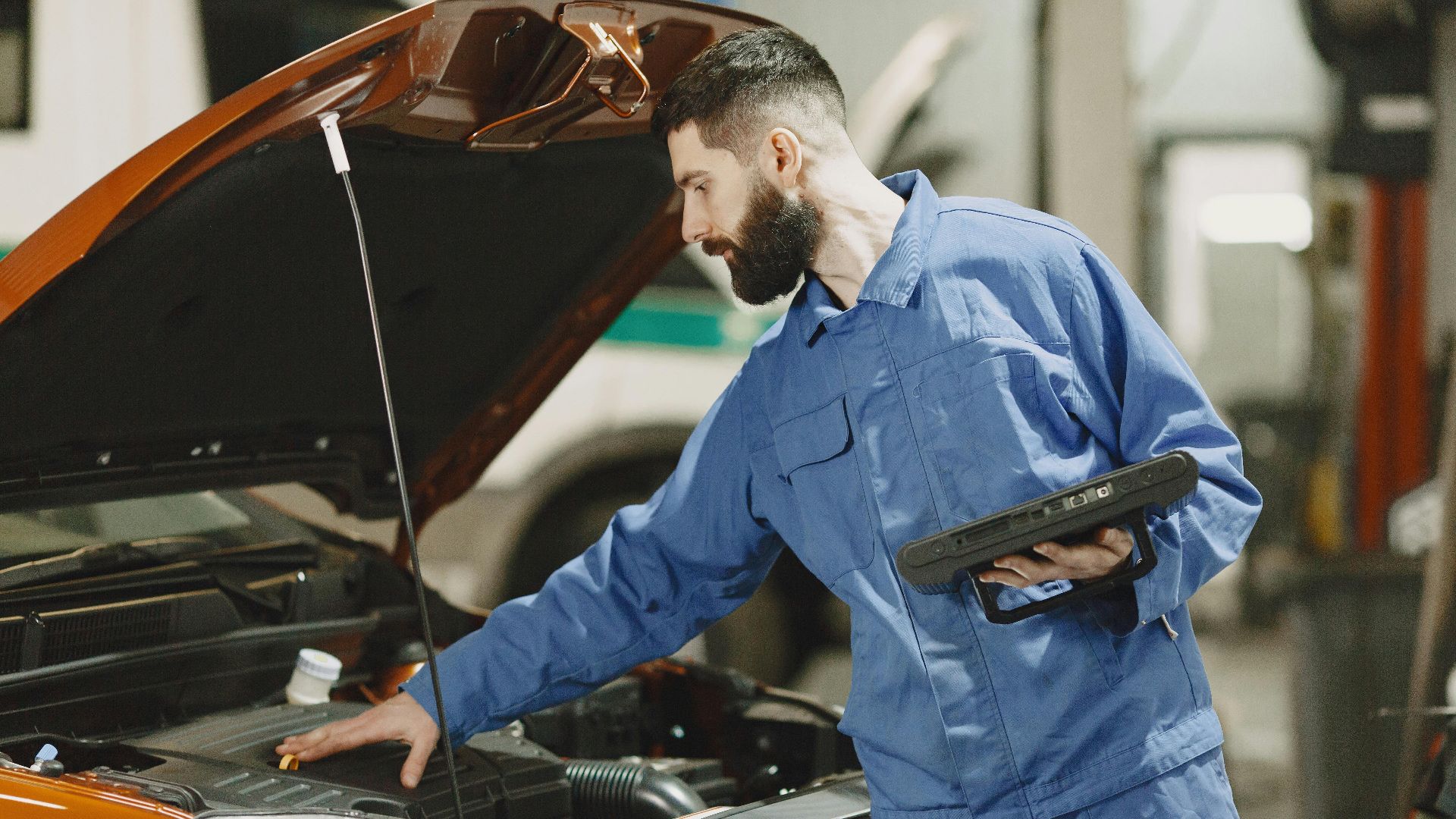 Professional mechanic examining a car engine under an open hood in a garage setting.