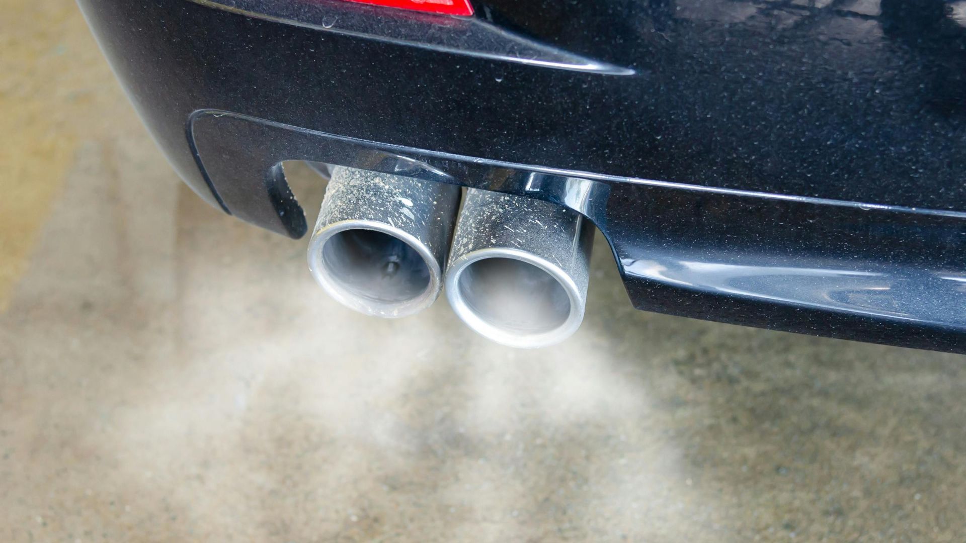 Close-up of a car's exhaust pipes emitting visible smoke, highlighting air pollution.
