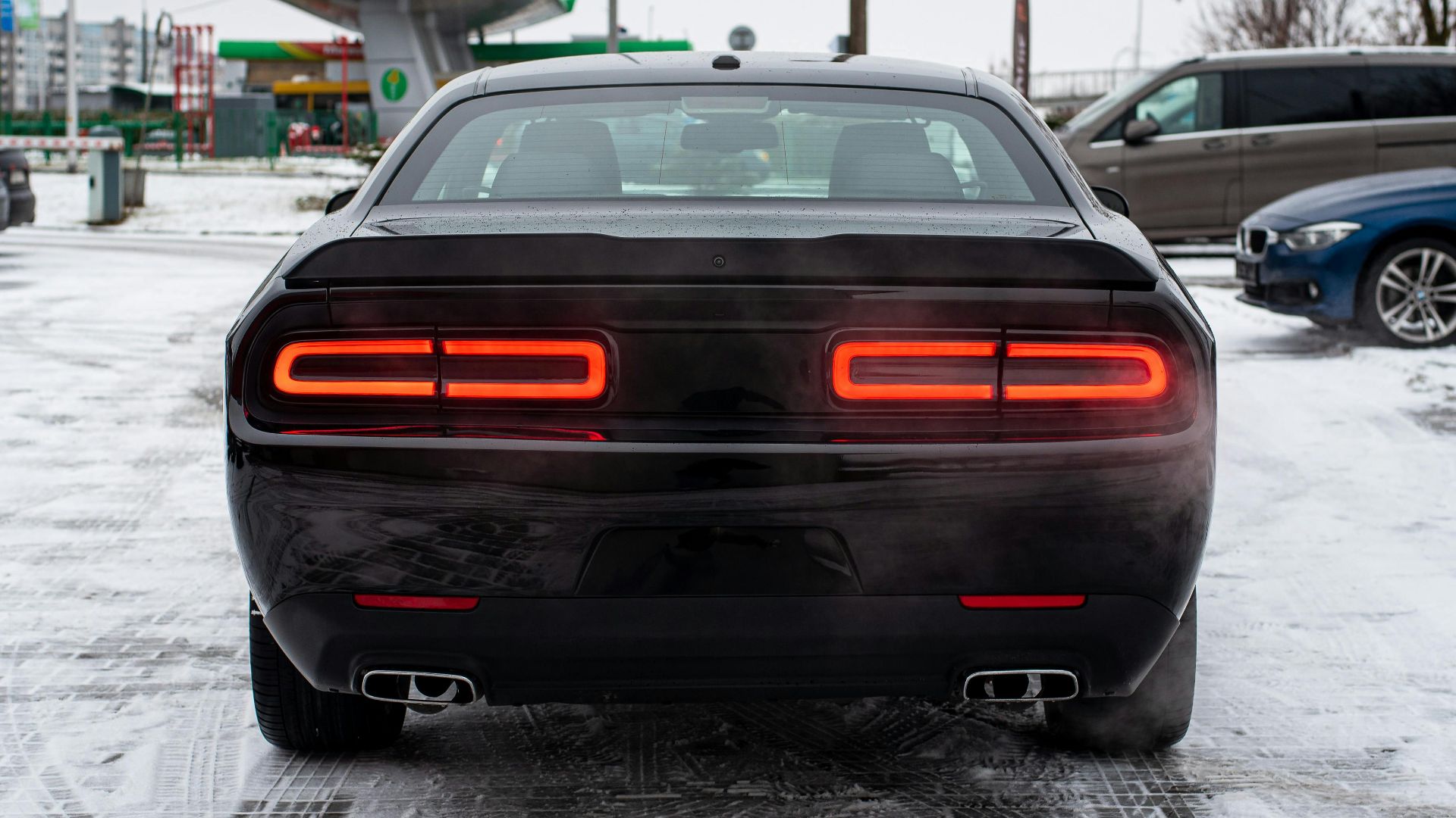 Black luxury car parked on a snow-covered ground at a gas station during winter.