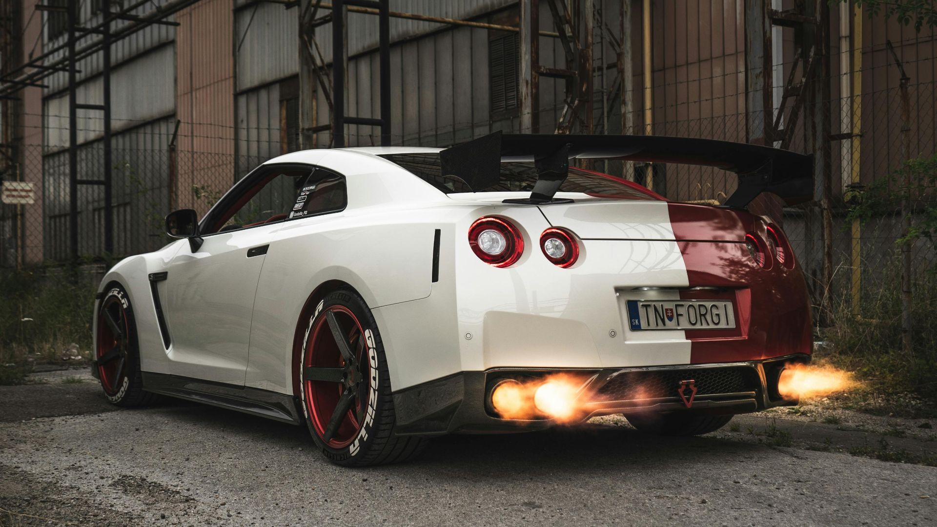 Back view of a powerful sports car emitting flames from its exhaust in an industrial urban area.