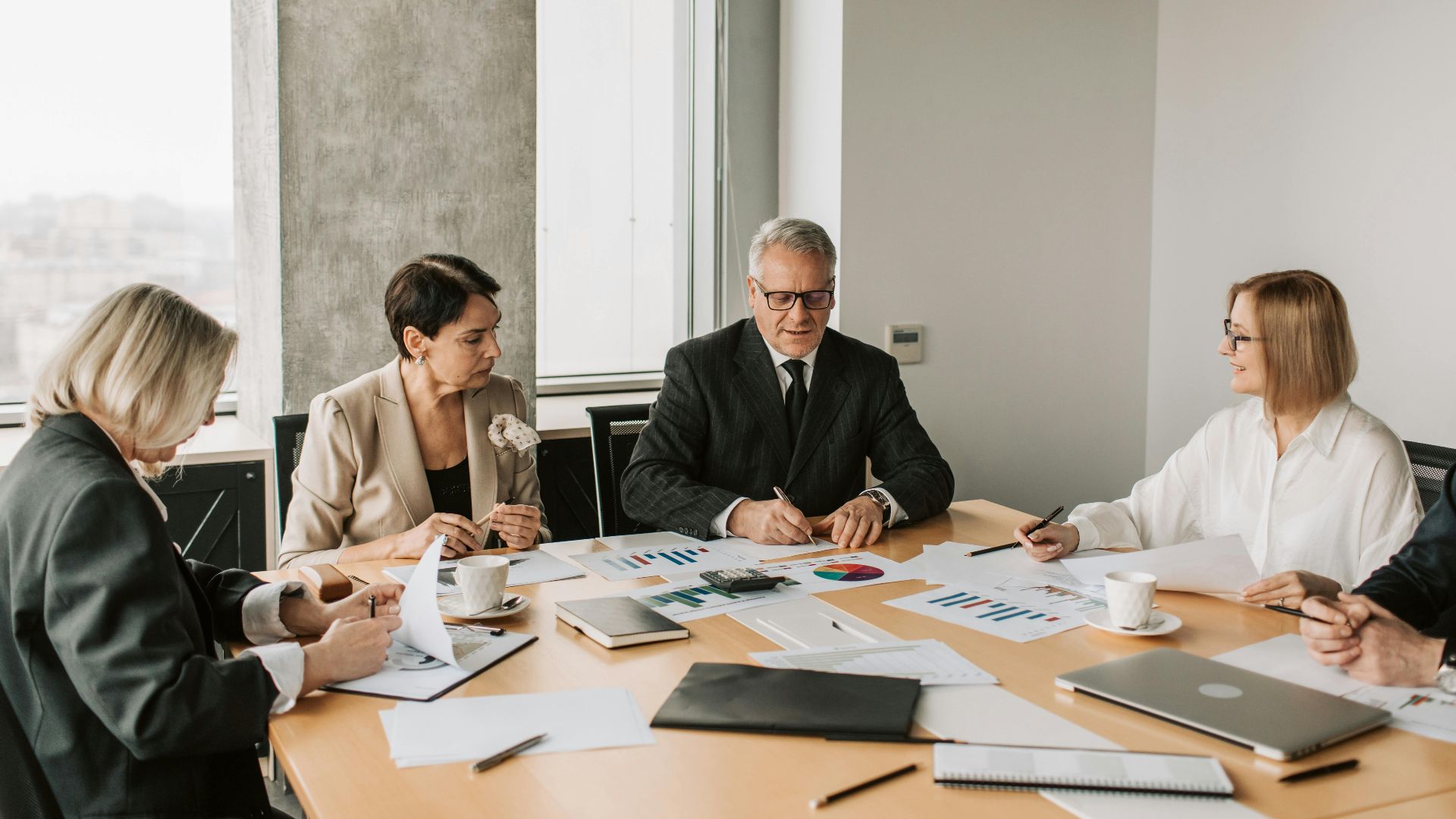 A group of professionals discussing business documents during a meeting in a modern office setting.